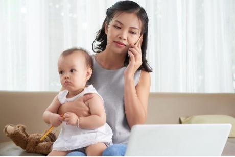 Mom holding baby while on phone and looking at laptop