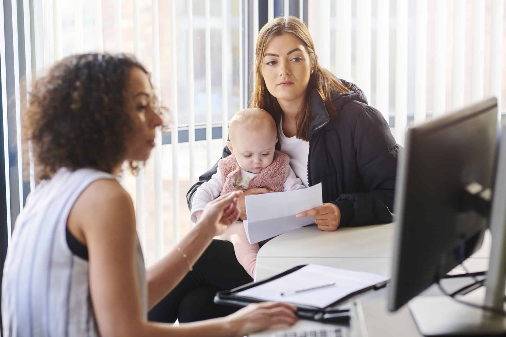 woman sitting at computer helping a woman and her baby