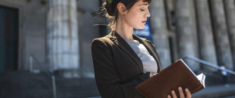 Woman looking at a legal text in front of courthouse