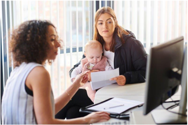mujer sentada frente a una computadora ayudando a una mujer y su bebe